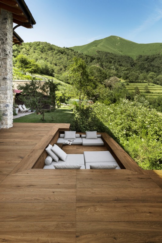 Terrassenplatten in dunkler Holzoptik mit Blick auf heller Sitzecke und grüne Bäume