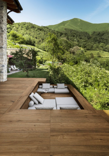 Terrassenplatten in dunkler Holzoptik mit Blick auf heller Sitzecke und grüne Bäume